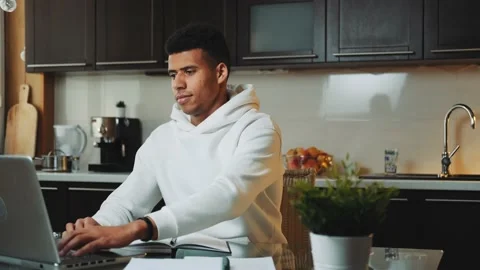 Tired black man exercising while working on the computer in the kitchen at home Stock Footage 131538734
