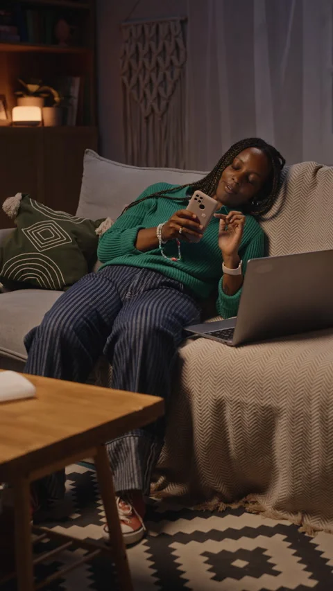 Tired Black Woman Scrolling on Smartphone with Laptop at Night Stock Footage 344120973