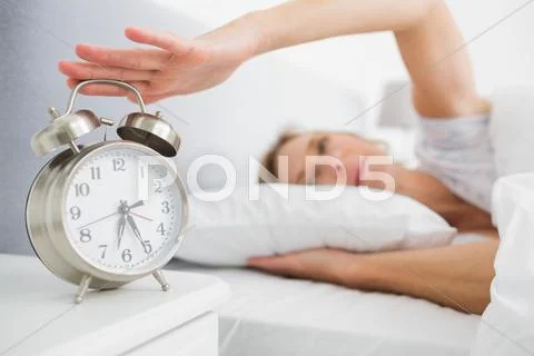 Tired blonde woman turning off her alarm in the morning Stock Photos