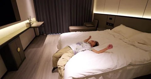 Tired boy coming and falling back onto a soft hotel bed, slow motion follow shot Stock Footage 322043824