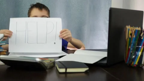 A tired boy at the table shows a sign that says help. I'm tired of studying at Stock Footage 144935112