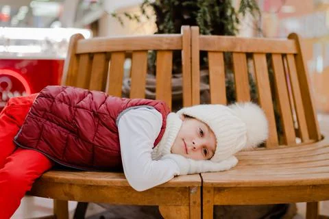 Tired boy in white bobble hat is lies with his mittened hands under his head on Stock Photos