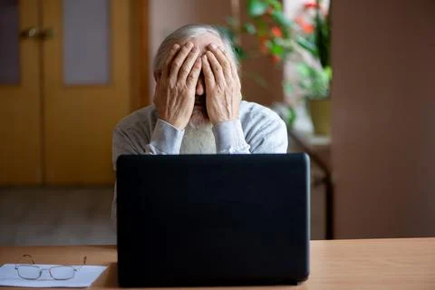 A tired, broken, resigned, preoccupied elderly man sits in front of a laptop, Stock Photos