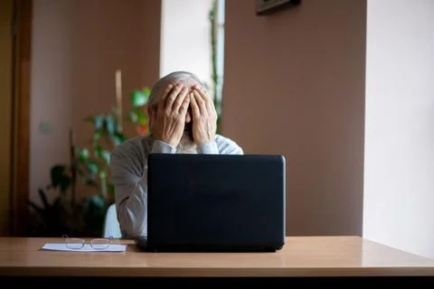 A tired, broken, resigned, preoccupied elderly man sits in front of a laptop, Stock Photos