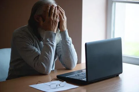 A tired, broken, resigned, preoccupied elderly man sits in front of a laptop, Foto stock