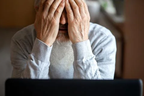 A tired, broken, resigned, preoccupied elderly man sits in front of a laptop, Stock Photos
