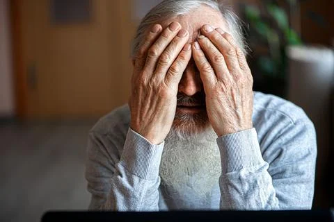 A tired, broken, resigned, preoccupied elderly man sits in front of a laptop, Stock Photos