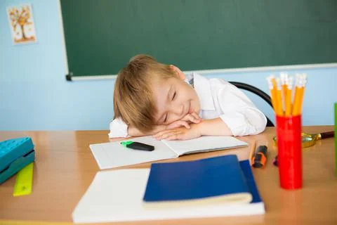 Tired child sleeping while studying in the primary school classroom. Difficult 스톡 사진