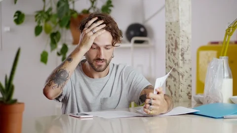 Tired clever guy sitting with papers calculating to solve life problems using Stock Footage 108797781
