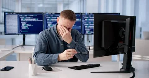 Tired Coder Rubs Irritated Eye During Extended Hours At Workstation Stock Photos
