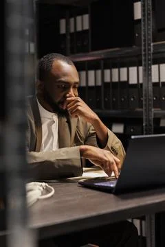 Tired cop thinking while solving case using laptop 库存照片