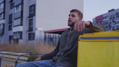A tired courier sits down exhausted on a bench outside after a work day Stock Footage 265062195