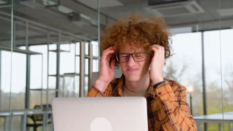 Tired disappointed programmer sitting at a table in office and working on a Stock Footage 221160633
