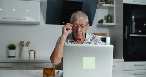 Tired Elderly man with glasses works on a laptop at home, takes off his glasses Stock Footage 146708366