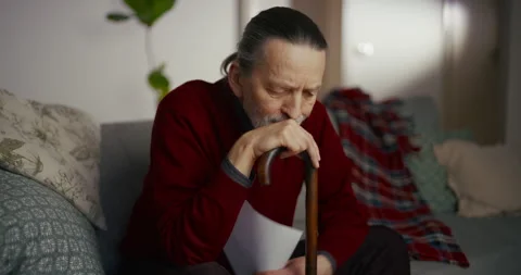 Tired elderly man sitting on sofa with cane in a calm home interior Vídeo Stock 336277379