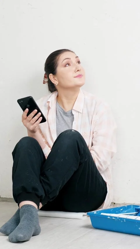 Tired female decorator taking a break from wall painting, scrolling on her phone Stock Footage 342912474