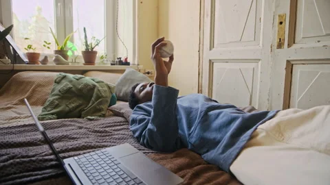 Tired Freelancer Throwing Baseball in Bed after Work on Laptop at Home Stock Footage 334796457
