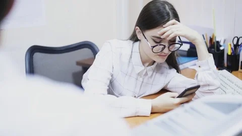 Tired Girl sitting with smartphone in office Stock Footage