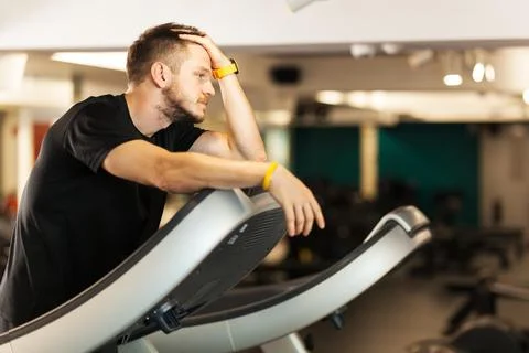 Tired guy walking on a treadmill. Exhausted man reating. Stockfoto's