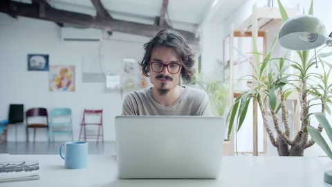 Tired hipster working on computer drinking from a cup a tea or coffee in loft Stock Footage 98895331