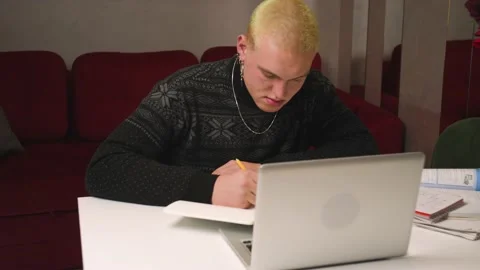 Tired homosexual man student using laptop write homework information in notebook Stock Footage 146907652