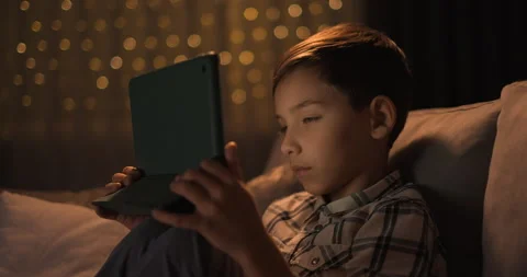 Tired kid falling asleep with gadjet in hands sitting on sofa at night Stock Footage 243093460