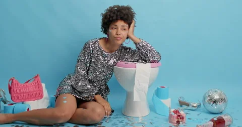 Tired lady with Afro hair wears glittering dress leans on toilet bowl poses in Stock Footage 157680053