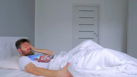 Tired Looking Young Man Gets Up Out of White Bed Sheets, Tracking Shot Stock Footage 133050589