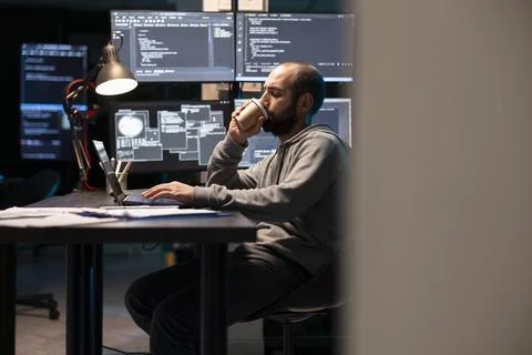Tired male programmer drinks hot beverage while typing on laptop Stock-Fotos