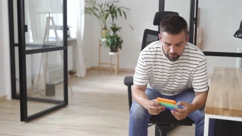 Tired male worker playing with push pop fidget toy in the office Stock Footage 233757989