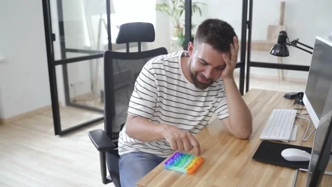 Tired male worker playing with push pop fidget toy in the office Stock Footage 233758329