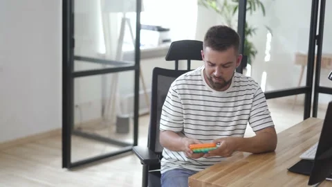 Tired male worker playing with push pop fidget toy in the office Stock Footage 233758604