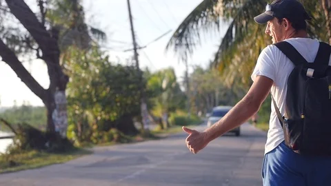 Tired man with a backpack behind him goes down the road at sunset, hitchhiking Video stock 94889438