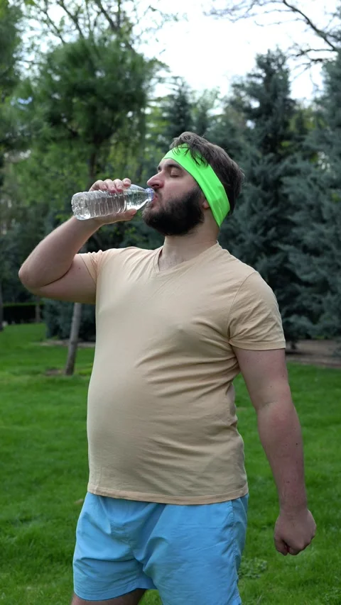 Tired man with beard drinks water from plastic bottle in park Stock Footage 306155564