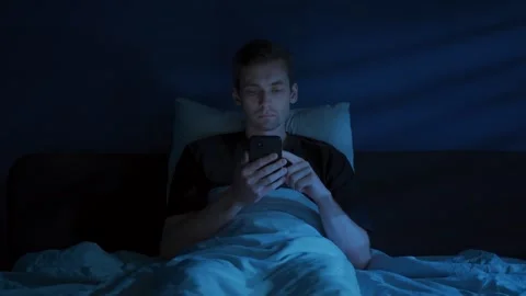 Tired Man Browsing Smartphone in Bed at Night 스톡 동영상 322780520