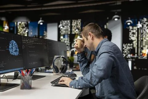 Tired man drinks coffee while utilizing AI on computer to optimize performance 写真素材