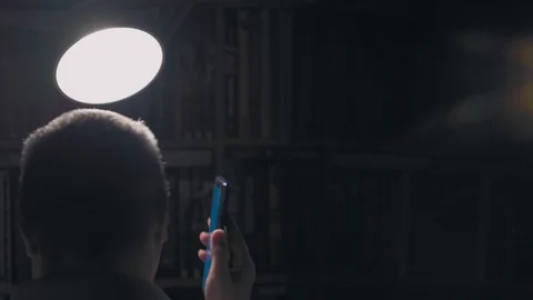 Tired man in face mask talks on the phone in dark room under lamp from back clos Stock Footage 128277736