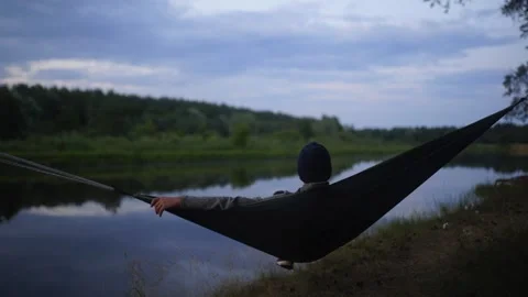 A tired man in a hat looking at river in a hammock Stock Footage 151130039