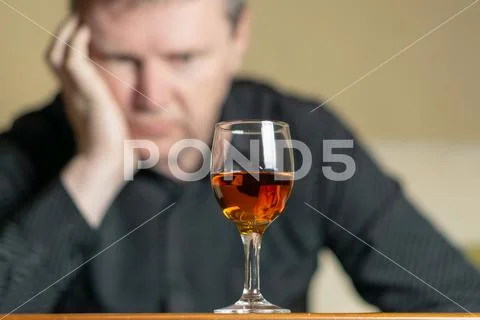 Tired man leaning his head on a glass of brandy. Man out of focus Stock Photos