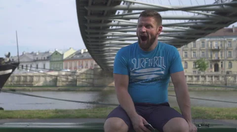 Tired man is looking around sitting on the bench against the river. Vídeo Stock 65188550