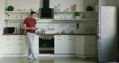 Tired Man is Putting Wireless Headset On, Listening Music in Kitchen Stock Footage 116479722