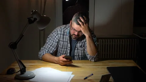 Tired man sits at a table and types on a smartphone 4K Stock Footage 130149407