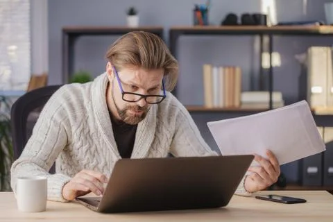 Tired man sitting at table with documents and laptop Stock Photos