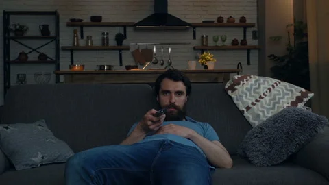 Tired man sitting on thew sofa at home after work. Holding remote control tv. Stock Footage 108612413