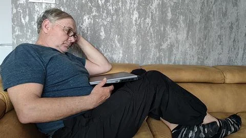 Tired man sleeping with laptop on sofa at home Stock Photos