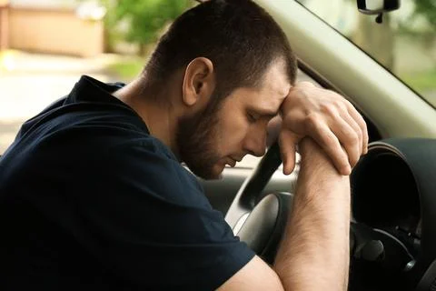 Tired man sleeping on steering wheel in his car Stock Photos