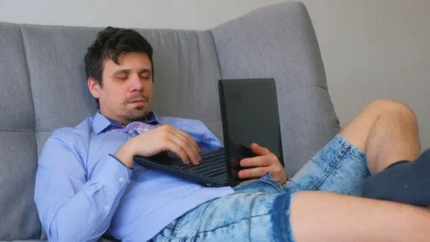 Tired man sleeps after working on laptop sitting on couch at home, distant work. Stock Footage 128968962