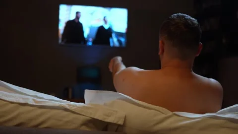 Tired man takes remote control to turn off TV and goes to sleep, rear view Vidéo 254005166