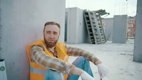 Tired man worker sitting and takes off white hardhat at construction workplace 動画素材 253589694