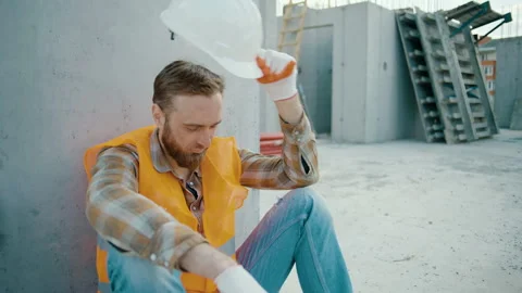 Tired man worker sitting and takes off white hardhat at construction workplace Video stock 258671033